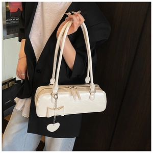 Detail of off-white glossy faux leather baguette bag with heart chain and bow charm