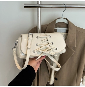 Detail of off-white glossy leather baguette bag with corset-style lace-up design and metal eyelets