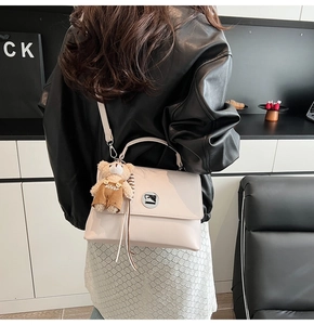 Detail of cream messenger bag featuring a metal lock and cute bear plush charm accessory