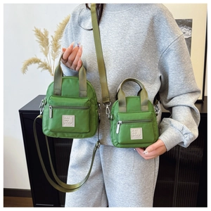 Detail showing two sizes of green waterproof nylon crossbody bags with logo and straps