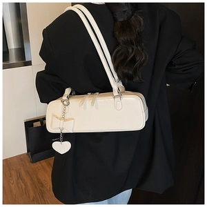 Detail of cream-white baguette bag featuring bow decoration and heart metal pendant