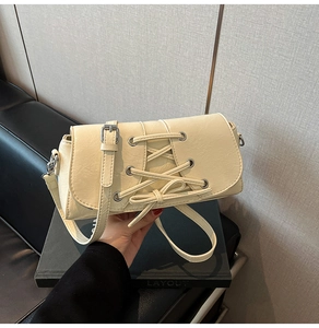 Detail of off-white crossbody bag featuring decorative lacing and silver eyelets