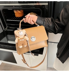 Close-up of caramel leather messenger bag with silver twist lock and cute bear charm