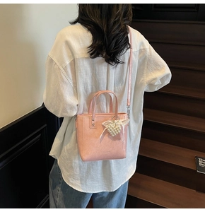 Détail d'un mini sac seau rose avec breloque cœur en perle porté par un mannequin