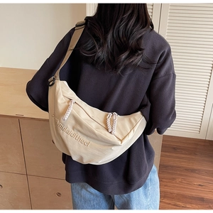 Detail of beige canvas crescent bag with wide nylon strap and elegant embroidery text