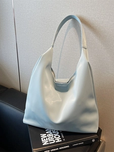 Chic mint green hobo bag with wide shoulder strap displayed on a modern black sofa