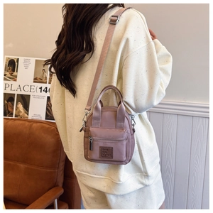 Dusty pink nylon crossbody bag shown in a lifestyle scene with adjustable strap and handles