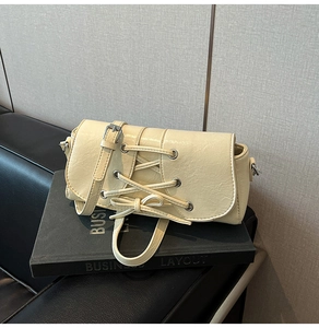 Detail of cream baguette bag featuring silver eyelet lacing and a stylish bow knot