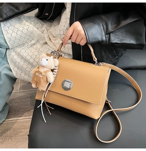 Detail of tan matte leather satchel with metal lock, featuring a cute plush bear pendant