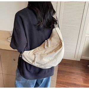 Detail of beige canvas dumpling bag featuring embroidered letters and dual woven zipper pulls