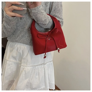 Détail du sac à main rouge verni avec nœud décoratif et pendentif papillon argenté