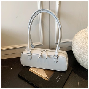 Detail of minimalist white baguette bag with silver zippers on a book and stone prop