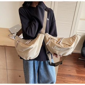 Detail of beige canvas crescent bag showing adjustable wide strap and letter embroidery