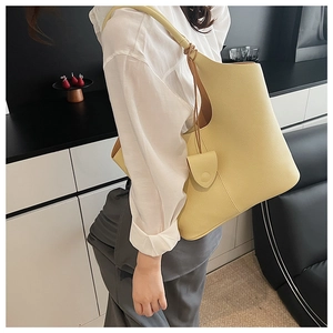 Detail view of the pale yellow litchi grain leather bucket bag with a side charm