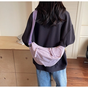 Rear view of a model wearing a light purple nylon crescent bag with embossed letters