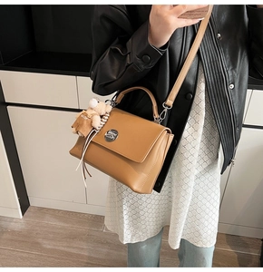 Detail view of a tan leather messenger bag with a round metal clasp and cute bear charm
