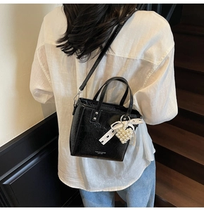 Détail du sac en cuir verni noir brillant avec breloque cœur perle et nœud en dentelle