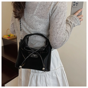 Détail d'un sac à main en cuir verni noir avec nœud et breloque en métal argenté