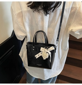 Détail du petit sac noir plissé brillant avec nœud en dentelle et pendentif cœur perlé