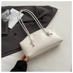 Close-up of white leather tote bag featuring decorative knots and metal end caps on straps