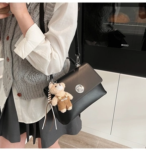 Detail of black leather crossbody bag with silver twist lock and teddy bear charm