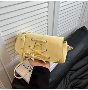 Detail of pale yellow crossbody bag with silver eyelets and corset-style lacing detail