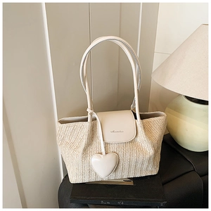 Detail of hand-woven straw tote bag with beige leather flap and heart pendant