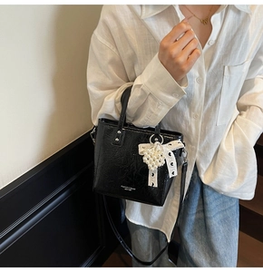 Détail du sac seau noir en cuir verni avec breloque perle en dentelle et bandoulière fine