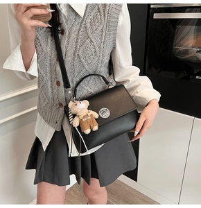 Detail of black crossbody bag with vintage metal lock and brown teddy bear charm