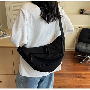 Detail of the black crescent crossbody bag showing textured fabric and wide shoulder strap