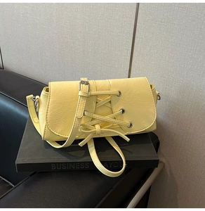 Detail showing bright yellow crossbody bag with silver eyelets and cross-tie texture