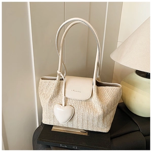 Detail of cream woven straw tote bag with leather flap and heart pendant on books