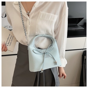 Détail d'un sac seau bleu clair en cuir avec nœud et bandoulière en chaîne métal