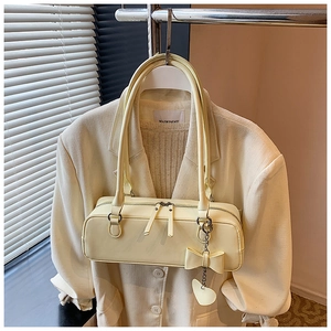Detail of cream yellow cylinder bag with bow charm hanging on a white blazer