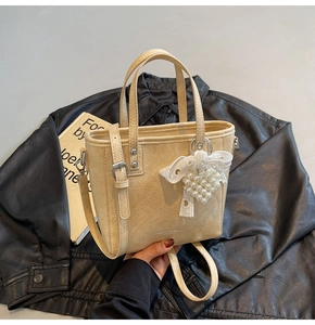 Détail d'un sac seau beige avec texture plissée et breloque cœur en perles et dentelle