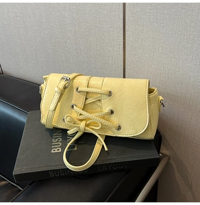 Detail of light yellow rectangular shoulder bag with lace-up corset design and bow