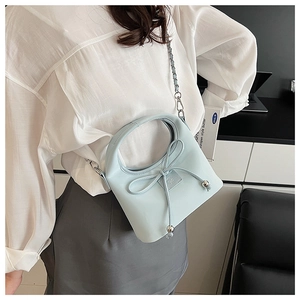 Détail d'un sac à main en cuir bleu clair avec nœud décoratif et bandoulière en chaîne