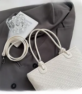 Detail of cream woven tote bag with detachable strap on a grey suit jacket background
