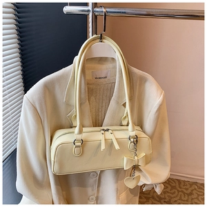 Detail of light yellow baguette bag featuring heart charm and metallic zipper closure