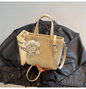 Détail du sac seau crème avec texture en cuir plissé et pendentif noeud en perles