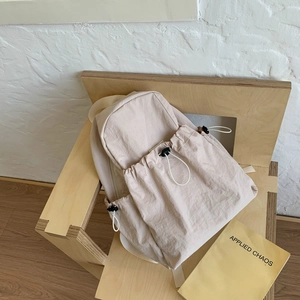 Detail of light beige nylon backpack featuring drawstring pockets and minimalist design