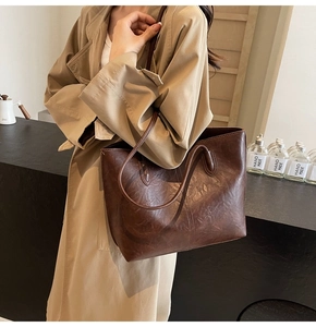 Detailed view of dark brown vintage textured leather tote bag on casual khaki trench coat