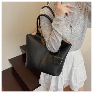 Side view of a black pebbled leather bucket bag with slim straps worn by a model