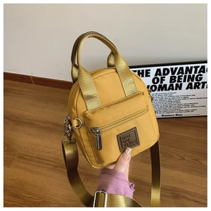 Detail of yellow waterproof nylon crossbody bag with leather brand logo and silver hardware