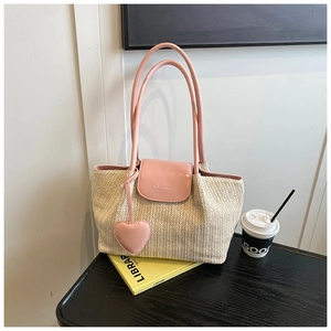 Detail of handwoven beige straw tote with pink leather flap and heart-shaped charm