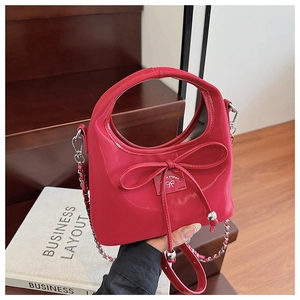 Détail d'un sac en cuir verni rouge avec un petit nœud et une bandoulière argentée