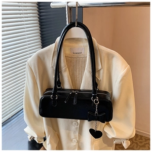 Detail view of black faux leather baguette bag with silver zippers and heart bow charm