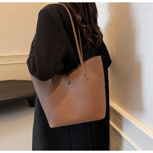 Detail of a large brown pebble leather tote bag with long straps worn by a model