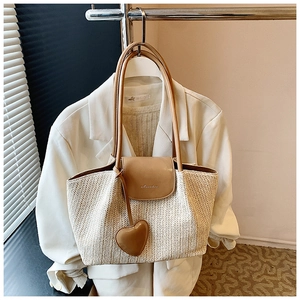 Detail of a large straw tote bag with brown faux leather trim and heart charm