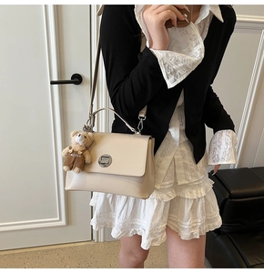 Detail of off-white leather square bag with metallic buckle and cute plush bear charm